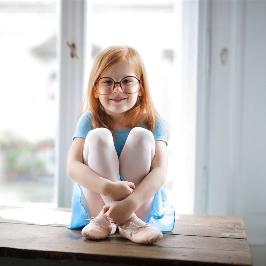 Niña pelirroja con gafas sentada en una mesa