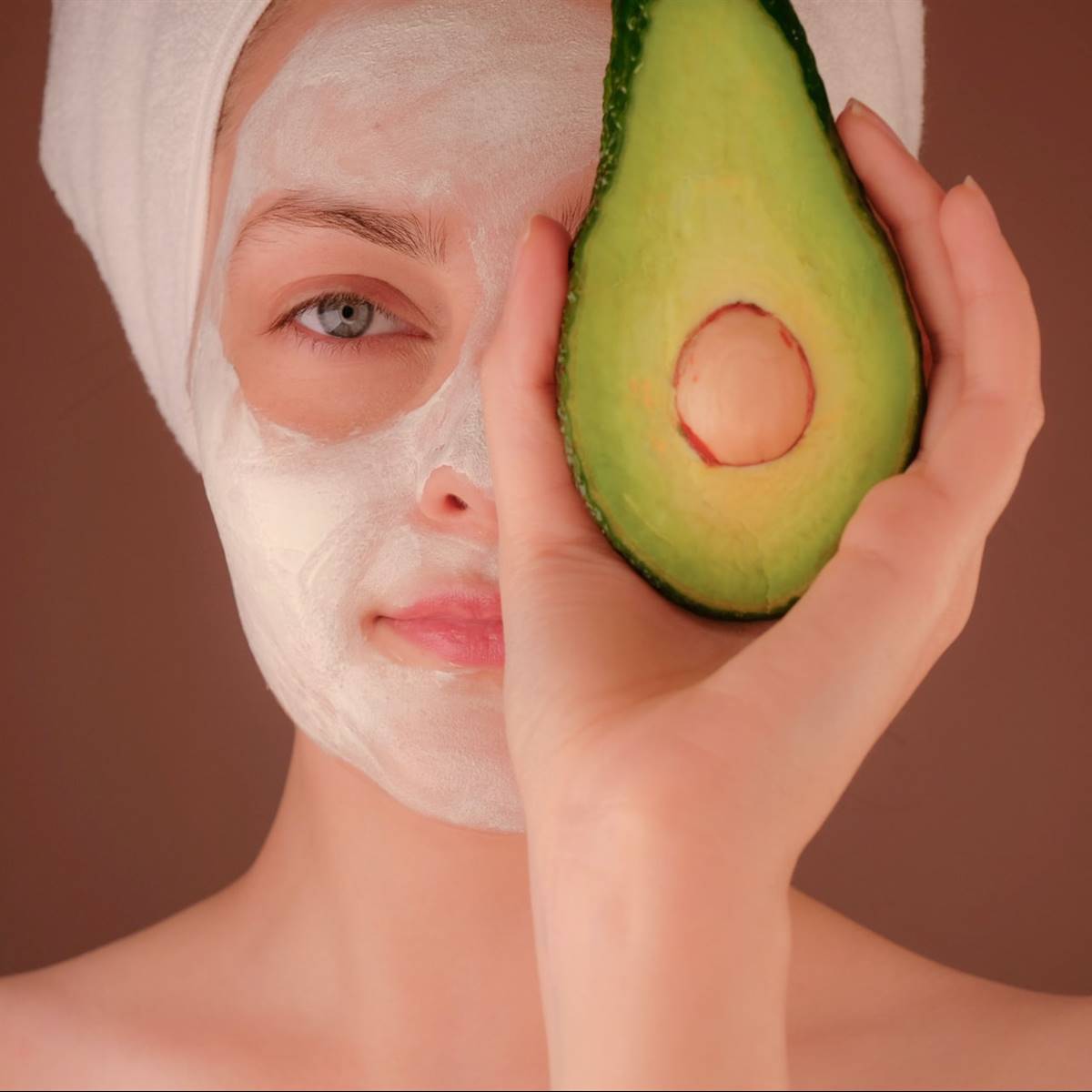 Mujer con mascarilla facial y un aguacate en la mano