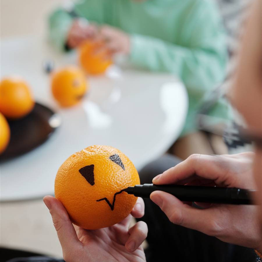 A man paints a tangerine as if it were a Halloween pumpkin