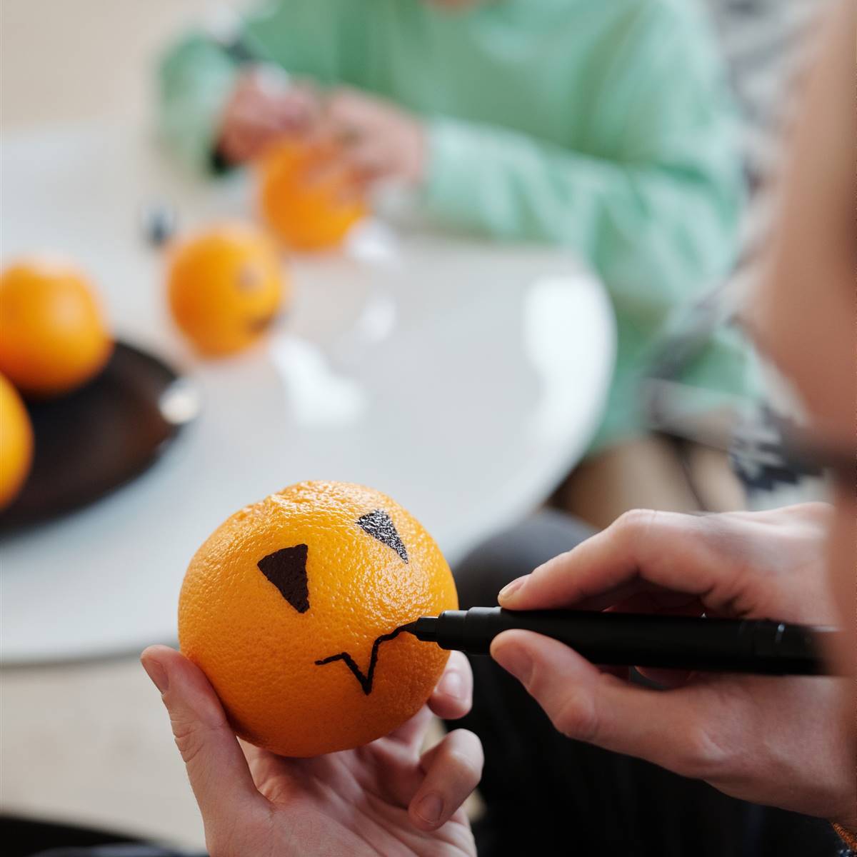 Hombre pintando una mandarina como si fuera una calabaza de Halloween