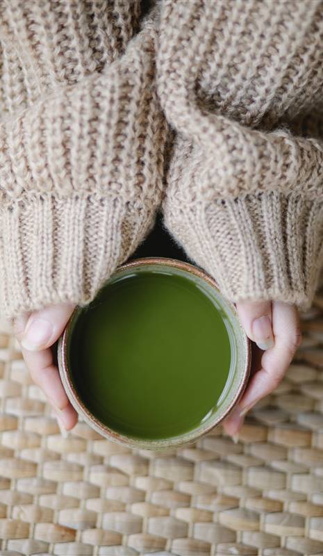 Manos de mujer sosteniendo un tazón de té verde