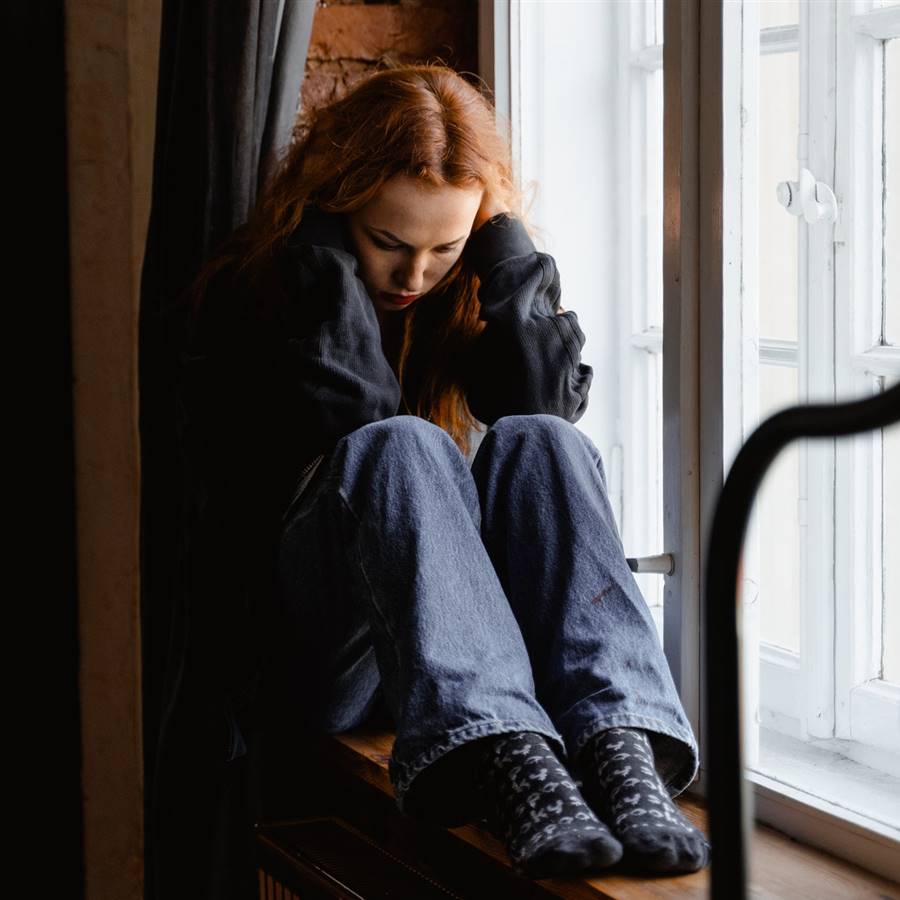 Chica cabizbaja sentada junto a una ventana