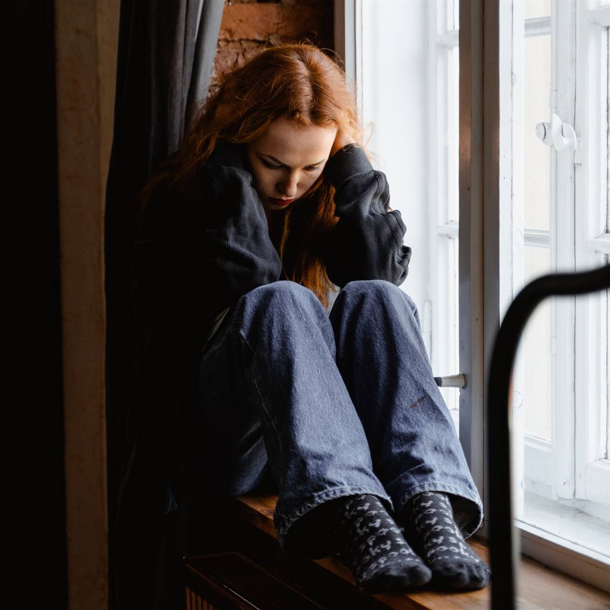 Chica cabizbaja sentada junto a una ventana