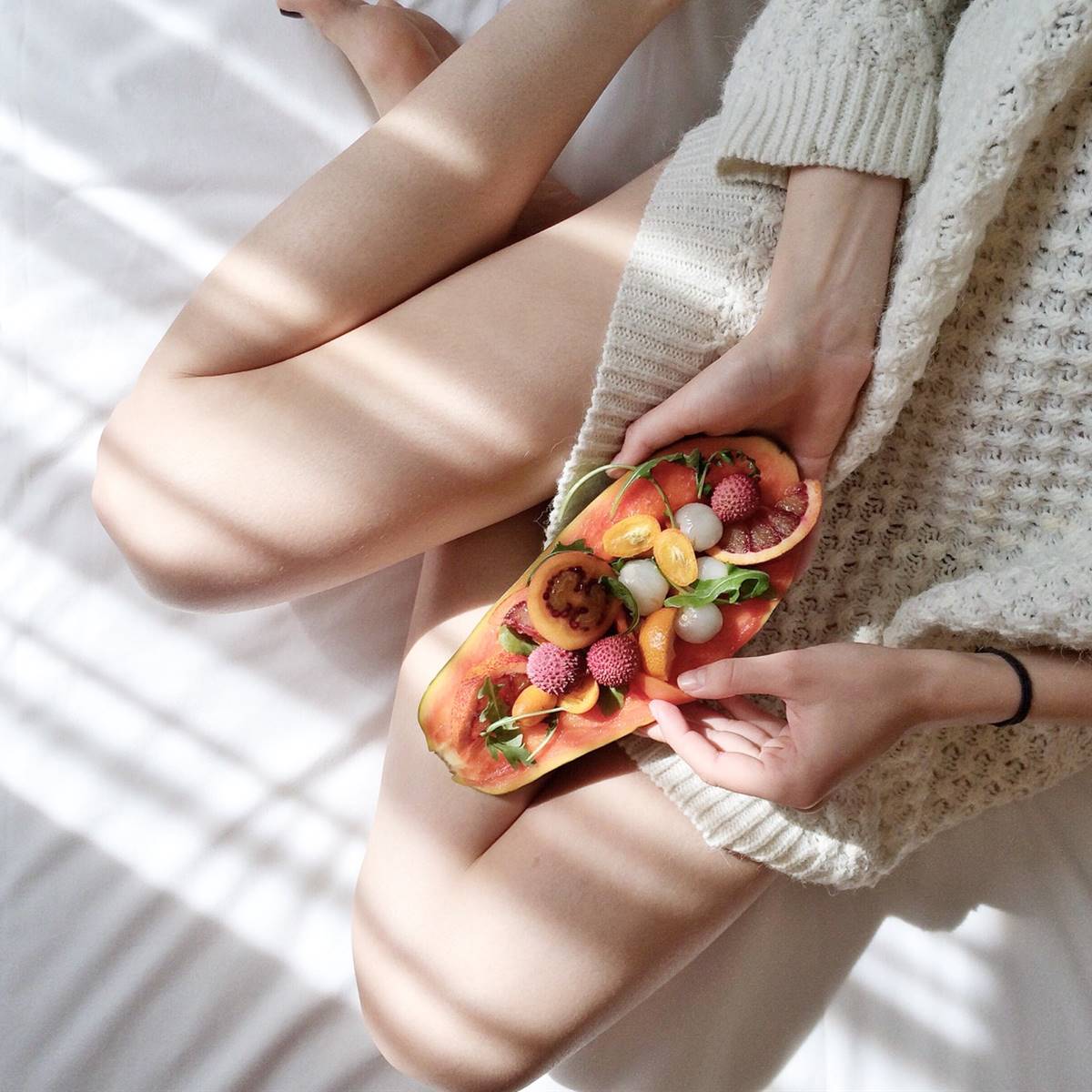 Mujer sentada comiendo una papaya rellena de otras frutas