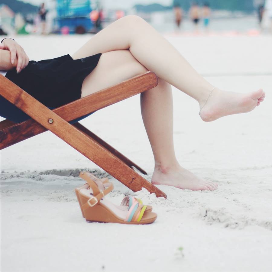 Mujer sentada en la playa con los pies descalzos