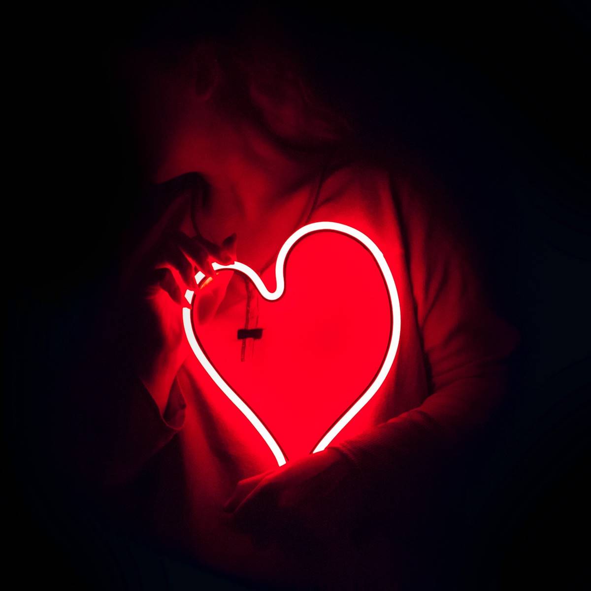 Mujer sosteniendo un neon en forma de corazón en la oscuridad