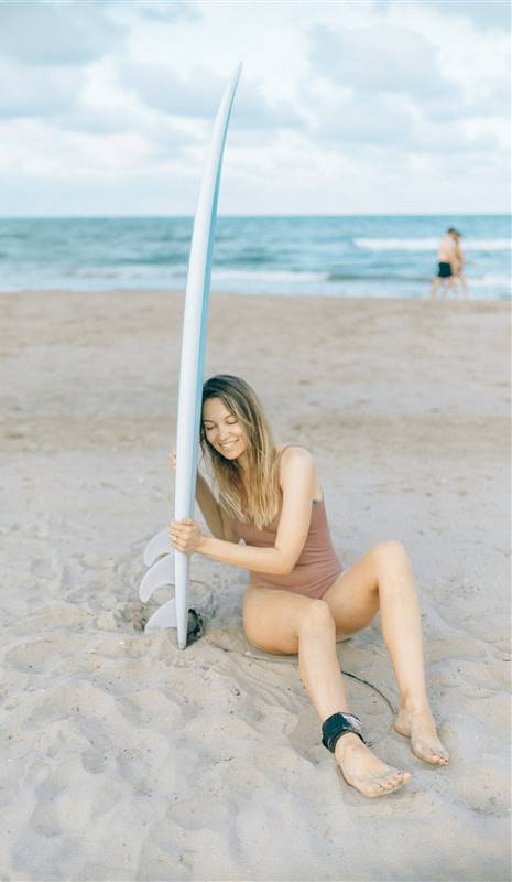 Mujer con tabla de surf sentada en la playa