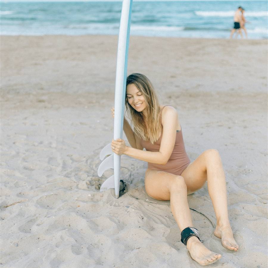 Mujer con tabla de surf sentada en la playa