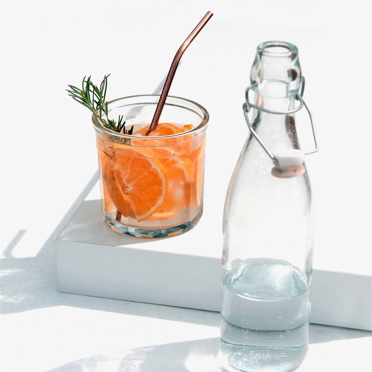 Vaso de agua con rodajas de naranja y rama de romero
