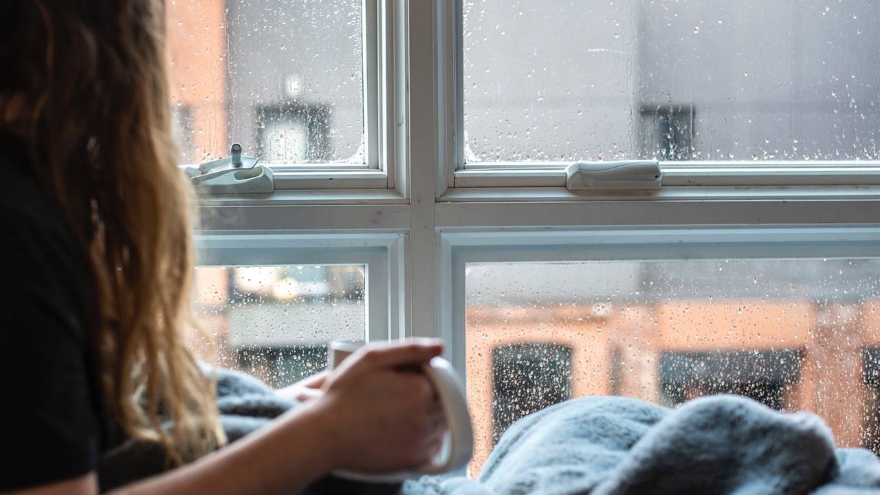 Chica con una taza viendo como llueve